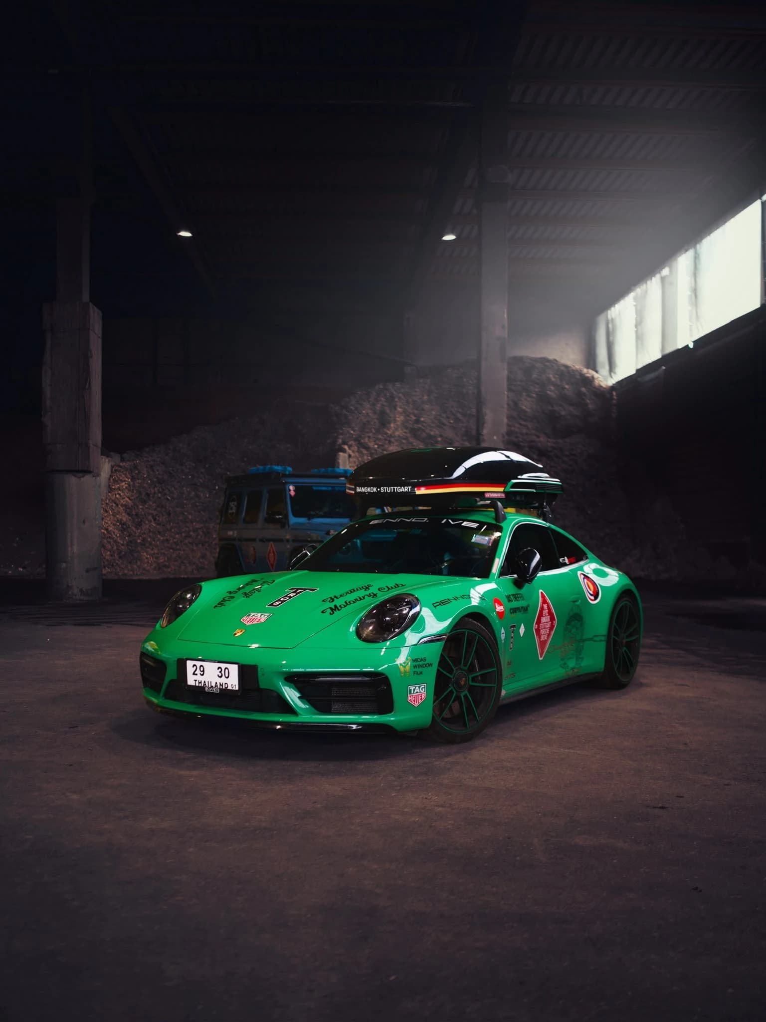 Grüner Sportwagen mit Dachbox in einer dunklen Industriehalle